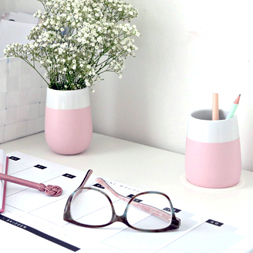 Ein weißer Schreibtisch mit rosafarbenen Behältern für Stifte.